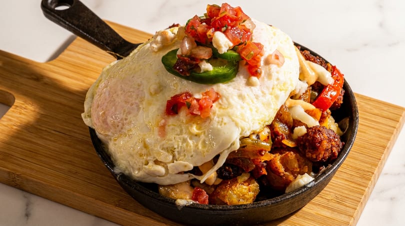 Breakfast skillet with fried eggs, salsa, jalapeños, and savory potatoes in a cast iron pan.